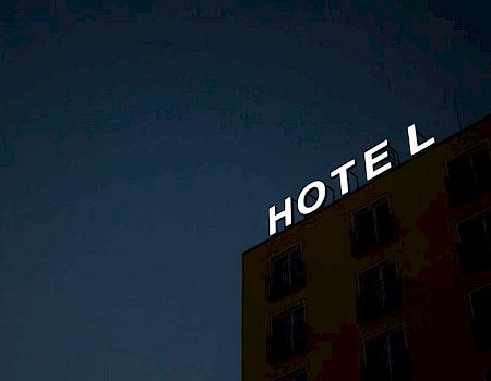 The image shows the exterior of a building at night, with illuminated letters spelling "HOTEL" on the rooftop.