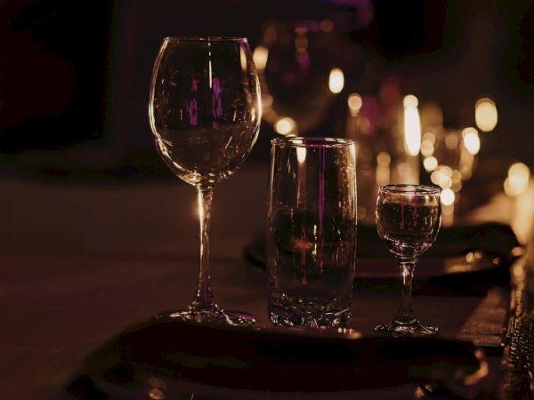 A dimly lit restaurant table with three wine glasses (red wine) and candles in the background, creating a warm, intimate dinner setting.
