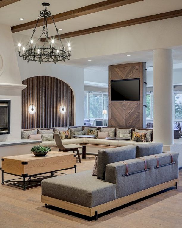 A spacious, modern living area with a large fireplace, seating arrangements, wooden flooring, a chandelier, and a wall-mounted TV.