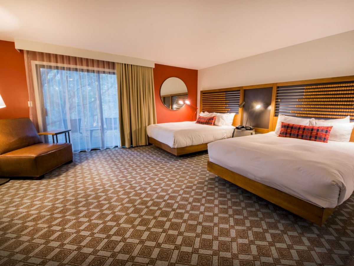 A hotel room with two double beds, a large window with curtains, a round mirror, armchair, side table, and two bedside lamps ends the sentence.