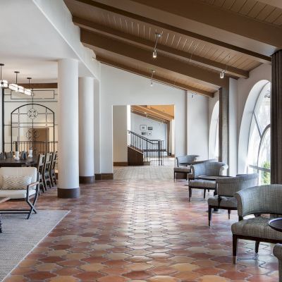 The image depicts a modern lounge area with arched windows, comfortable seating, and a mix of wooden and tiled flooring in a well-lit setting.