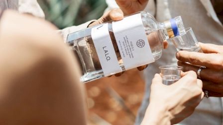 Several people pouring shots from a bottle labeled PENT... into small glasses, sharing a drink outdoors.