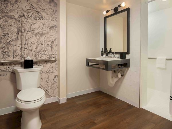A modern bathroom with a wall-mounted sink, a black-framed mirror, a white toilet, and a patterned feature wall behind the toilet, all on wooden flooring.