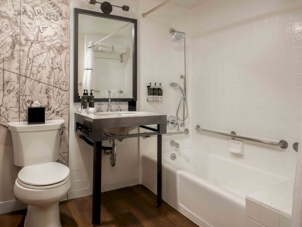 A modern bathroom with a toilet, a dark vanity sink, a mirror, and a white bathtub/shower combo, wood-like flooring, and a patterned wall.