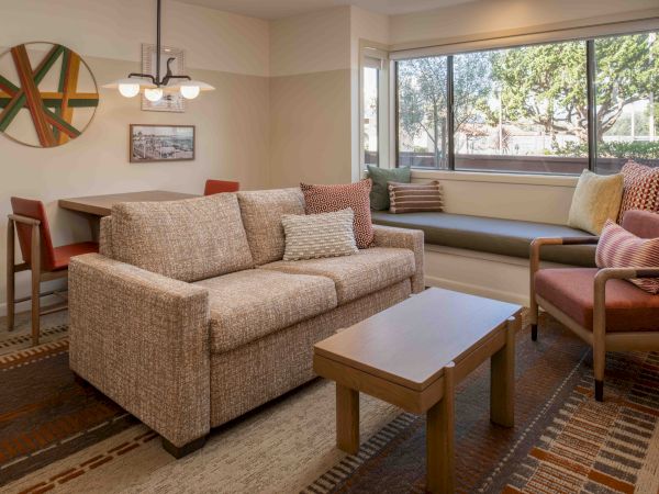A cozy living room with a beige sofa, armchairs, coffee table, and large window seating by the window. Top it at 140 characters, always ending the sentence.