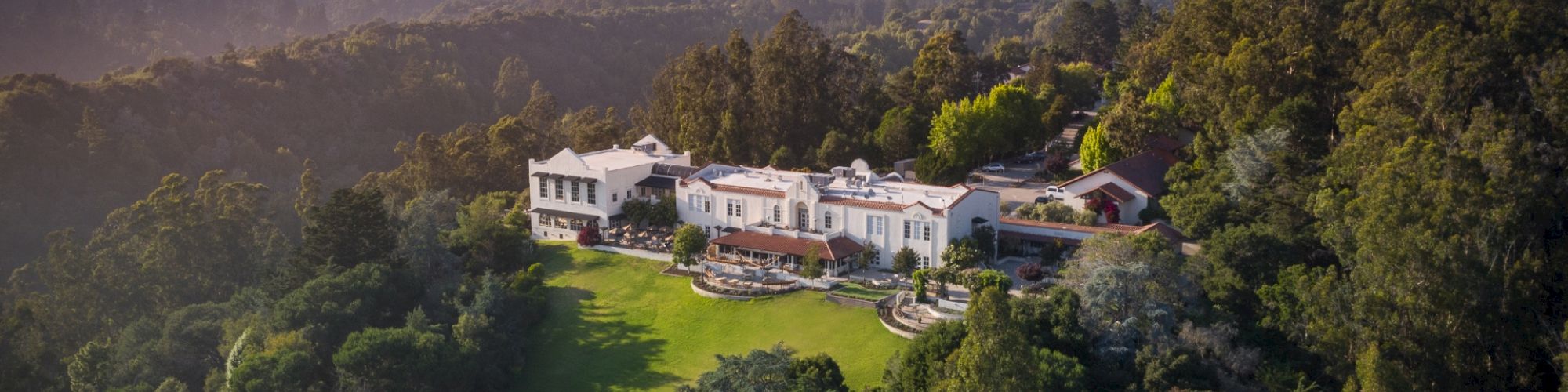 Aerial view of a large, luxurious estate surrounded by lush greenery and trees, with expansive grounds and multiple buildings.