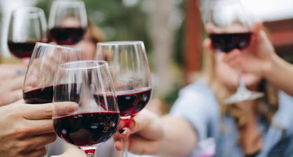 A group of people is raising glasses of red wine in a celebratory toast, suggesting a festive or social gathering.