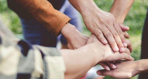 Several hands are stacked on top of each other, symbolizing unity, teamwork, or collaboration.