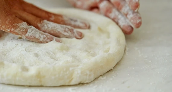 A person shaping a circular piece of dough with floured hands on a white surface.