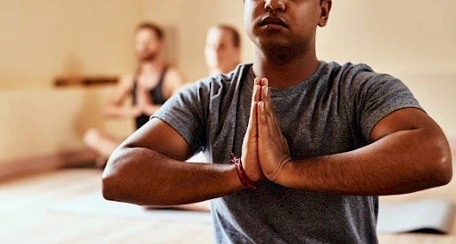 People practicing yoga in a class, focusing on meditation with hands in a prayer position, creating a calm and serene environment.