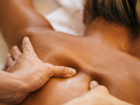 A person receiving a back massage, with hands applying pressure to the upper back area near the shoulder blades.