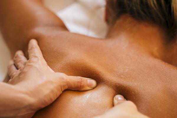 A person receiving a back massage, with hands applying pressure to the upper back area near the shoulder blades.