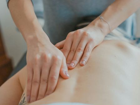 A person is receiving a back massage from another person whose hands are positioned on their back in a massage setting.