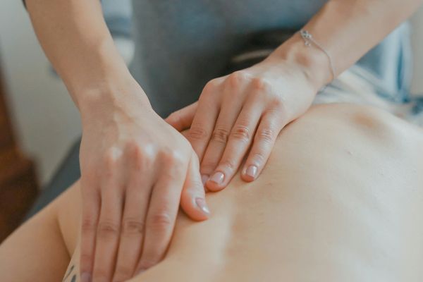 A person is receiving a back massage from another person whose hands are positioned on their back in a massage setting.