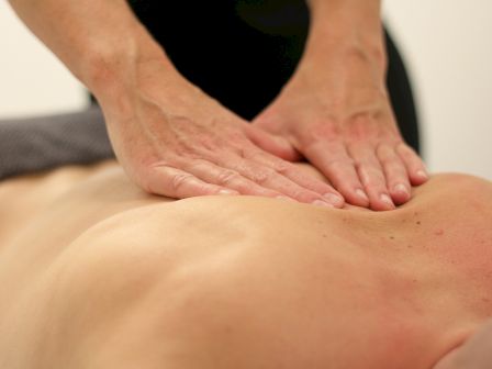 The image shows a person receiving a massage, with hands pressing and kneading the back muscles. The setting appears to be a spa or similar.