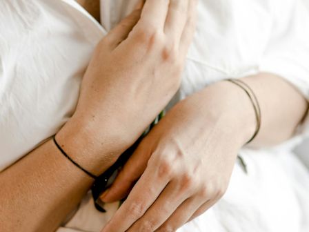 A person in a white shirt is holding some green plants close to their chest, showcasing their hands and part of their torso.