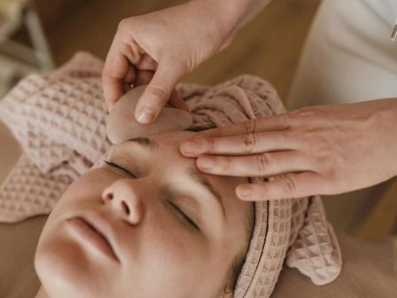 A person with a towel wrapped around their head is receiving a relaxing facial massage or treatment in a serene setting.