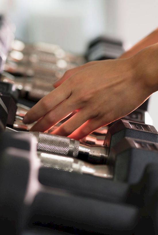 A person is selecting a dumbbell from a rack in a gym or fitness center.