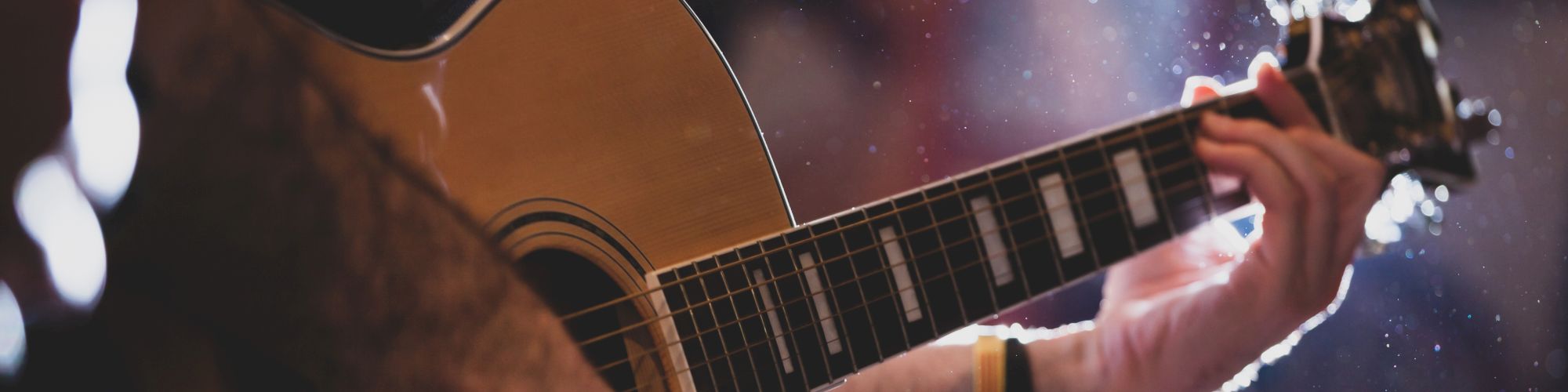 A person playing an acoustic guitar with a focus on the strings and the hands in a softly lit environment.