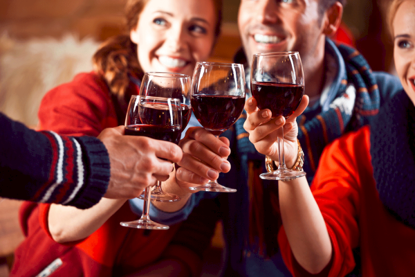 A group of people is raising and clinking glasses of red wine in a cheerful toast. They appear happy and are enjoying their time together.