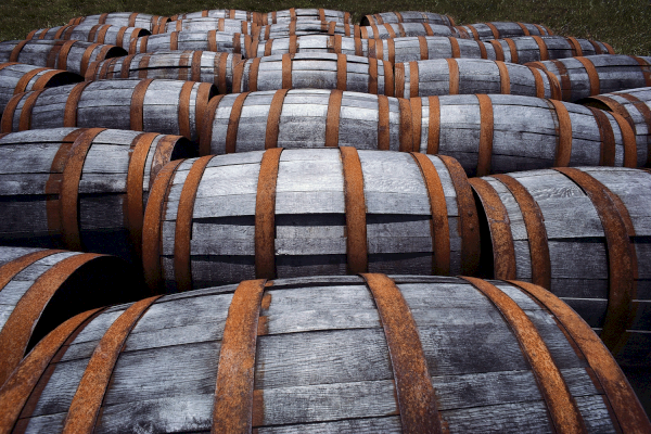 The image shows a collection of wooden barrels with metal bands, arranged closely together, likely used for storing or aging liquids, like wine or whiskey.