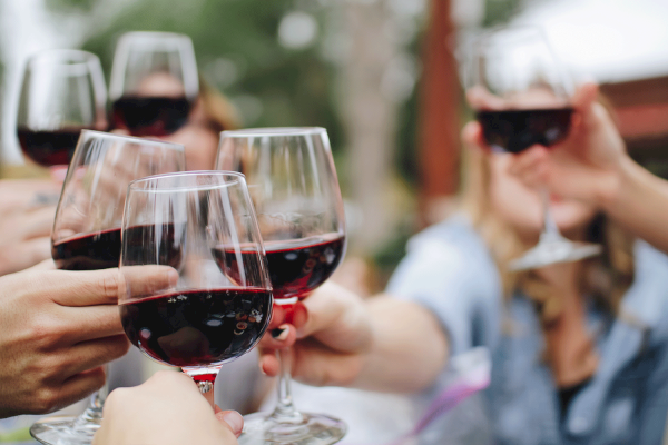 People toasting with glasses of red wine in an outdoor setting.