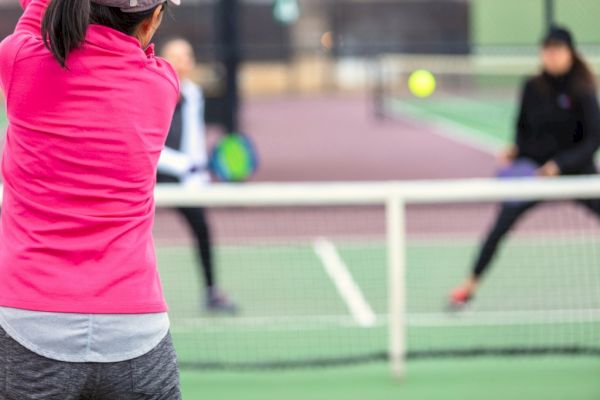 Three people are playing pickleball on an outdoor court, with one player preparing to hit the ball.