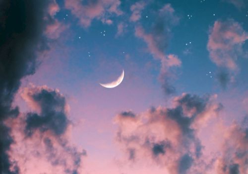 A crescent moon shining amid scattered clouds and twinkling stars in a colorful twilight sky.