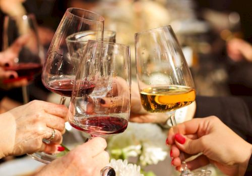 Several hands holding wine glasses in a toast, with both red and white wine visible.