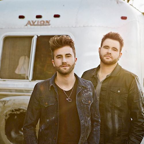 Two men stand in front of a silver trailer labeled 