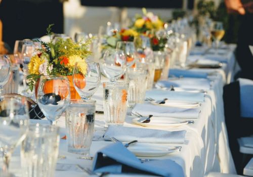 A long, elegantly set dining table with white tablecloths, glassware, silverware, and floral centerpieces, ready for a formal event or gathering.