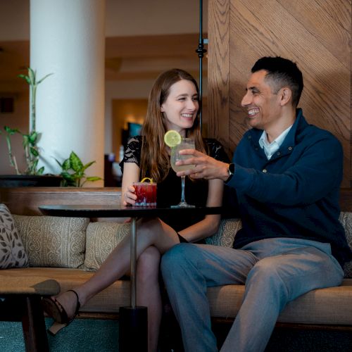Two people sharing a drink and smiles at a cozy bar, chatting and enjoying a night out together.