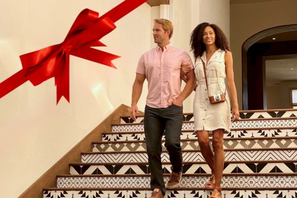 A couple descends ornately patterned stairs, with a large red ribbon decoration on the wall beside them.