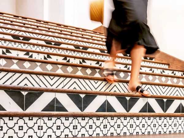 A person wearing a black skirt descends ornate, patterned stairs with wooden edges.