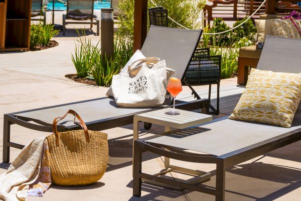 The image shows two poolside lounge chairs with bags, a pillow, and a drink, suggesting a relaxing outdoor setting near a pool.