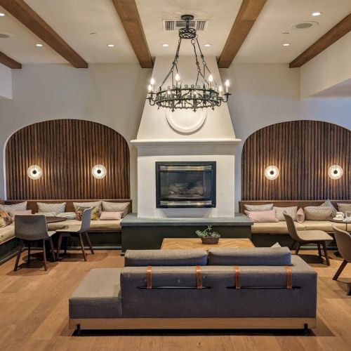 This image shows a modern, cozy lounge with a fireplace, elegant chandelier, wood accents, and comfortable seating areas.