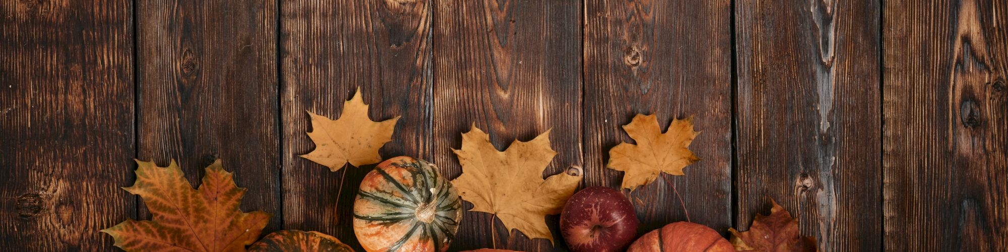 The image shows pumpkins, apples, and autumn leaves on a wooden surface, creating a rustic fall-themed scene.