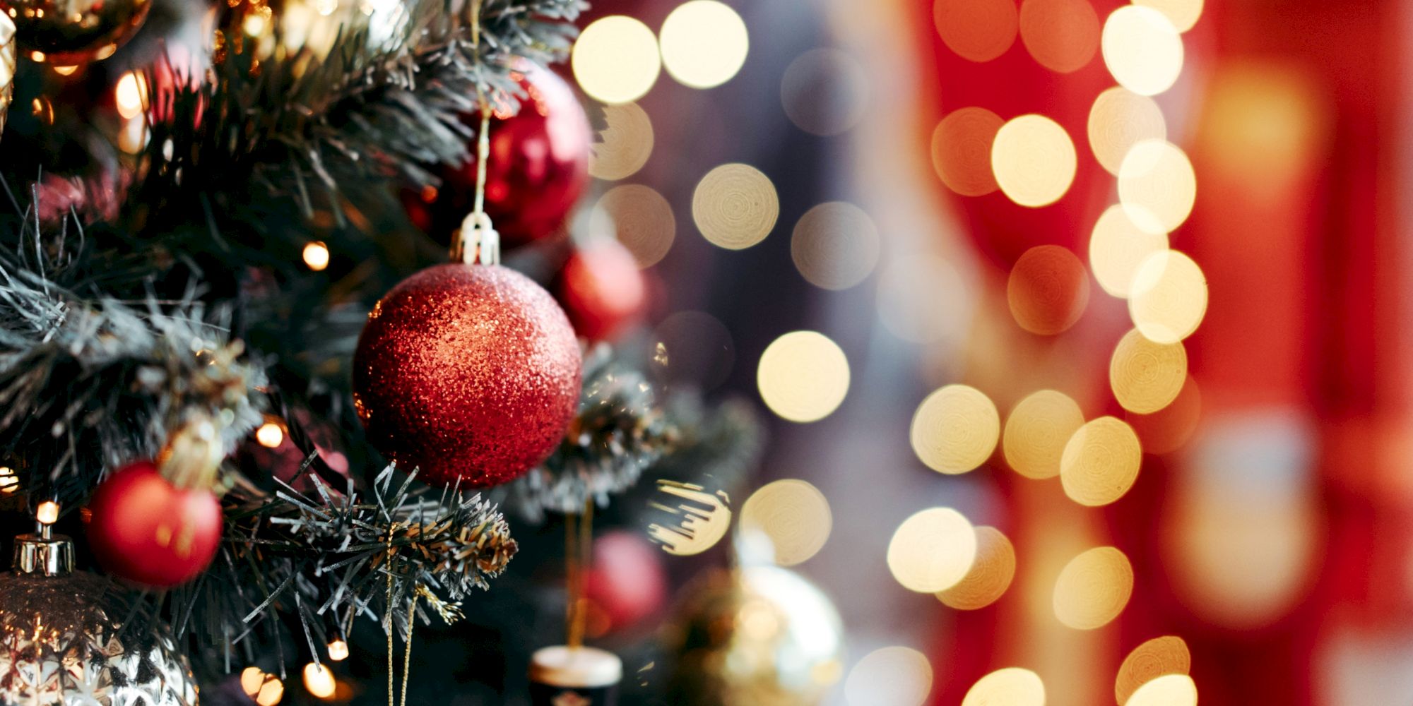 A decorated Christmas tree with red baubles and festive lights. The background shows out-of-focus, warm bokeh lights.