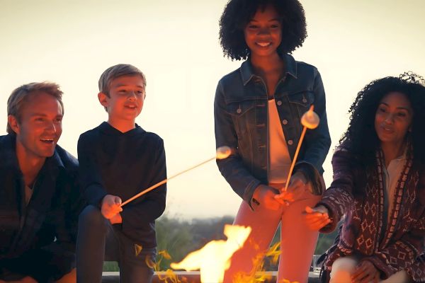 A group of people are roasting marshmallows over a campfire, enjoying an outdoor activity together as they smile and interact.