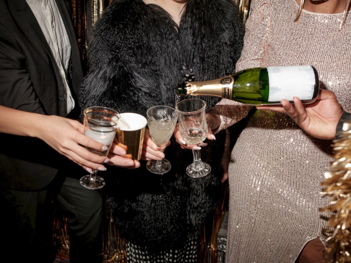 People dressed for a celebration are seen pouring champagne into glasses, ready to toast.