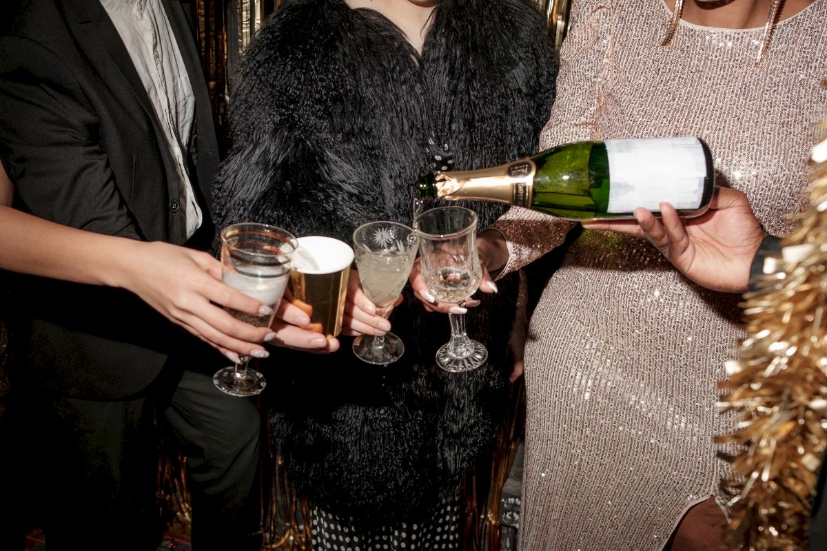 People at a party pouring champagne into glasses, dressed in fancy attire, with a festive atmosphere.