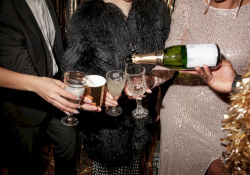 People at a party pouring champagne into glasses, dressed in formal attire with festive decorations in the background.