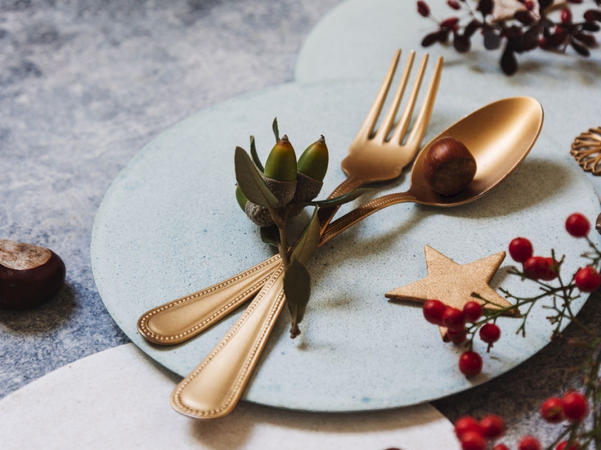 Gold utensils on a plate with decorative foliage, a chestnut, and red berries. A small wooden star adds to the arrangement’s charm.