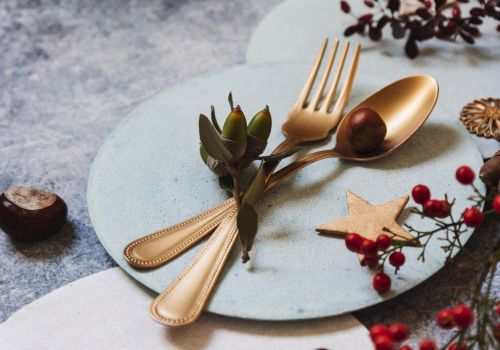 A decorative arrangement with golden cutlery, a chestnut, and festive elements like berries and a star on a plate.