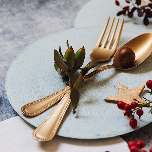 A decorative arrangement with golden cutlery, a chestnut, and festive elements like berries and a star on a plate.