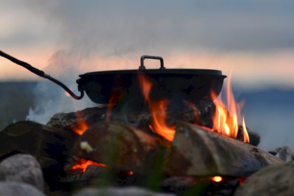 A pot is cooking over an open flame, surrounded by rocks with a scenic background.