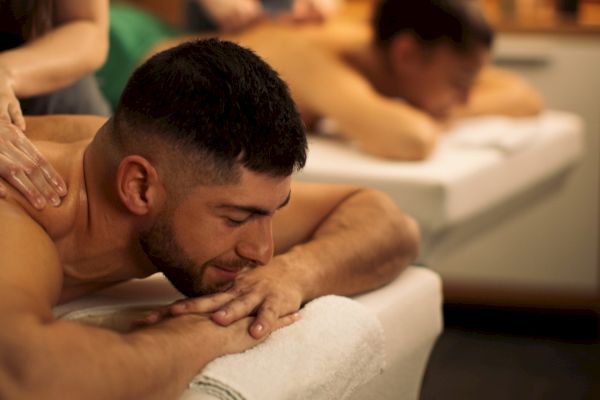 Two people relaxing on massage tables, receiving massages in a serene spa setting with candles in the background.