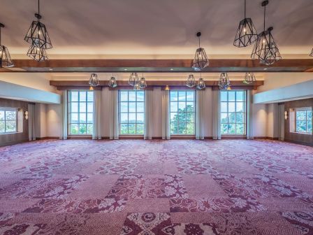 An empty room with large windows, floral carpet, and hanging geometric light fixtures, creating a spacious and bright atmosphere.