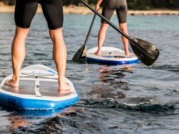 Two people are paddleboarding on a calm body of water, with a clear sky and distant shoreline visible in the background.