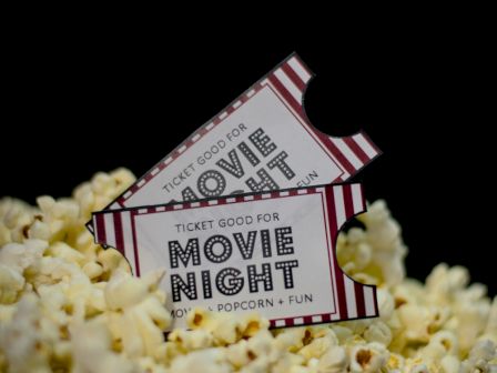 The image shows two "Movie Night" tickets on a pile of popcorn, suggesting an event of films, popcorn, and fun.